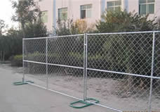 Two pieces of chain l<em></em>ink portable fence panel with vertical and horizo<em></em>ntal cross bars are fixed on the ground by two green me<em></em>tal feet.